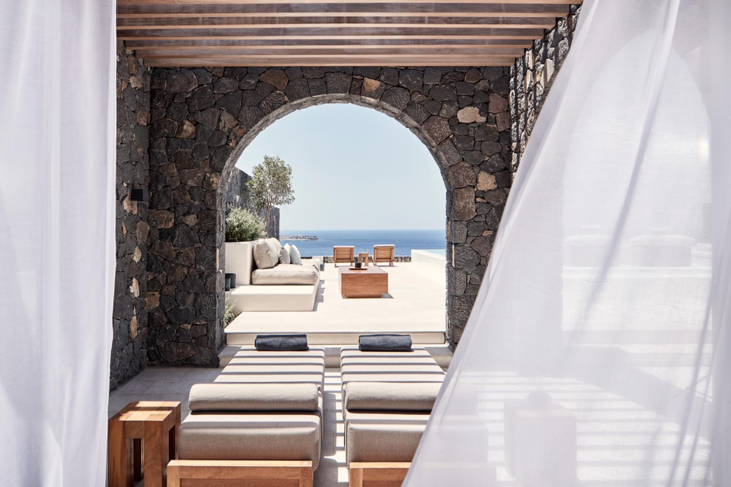 Stone-arched suite terrace with sea-view daybeds at Canaves Oia luxury hotel in Santorini, Greece