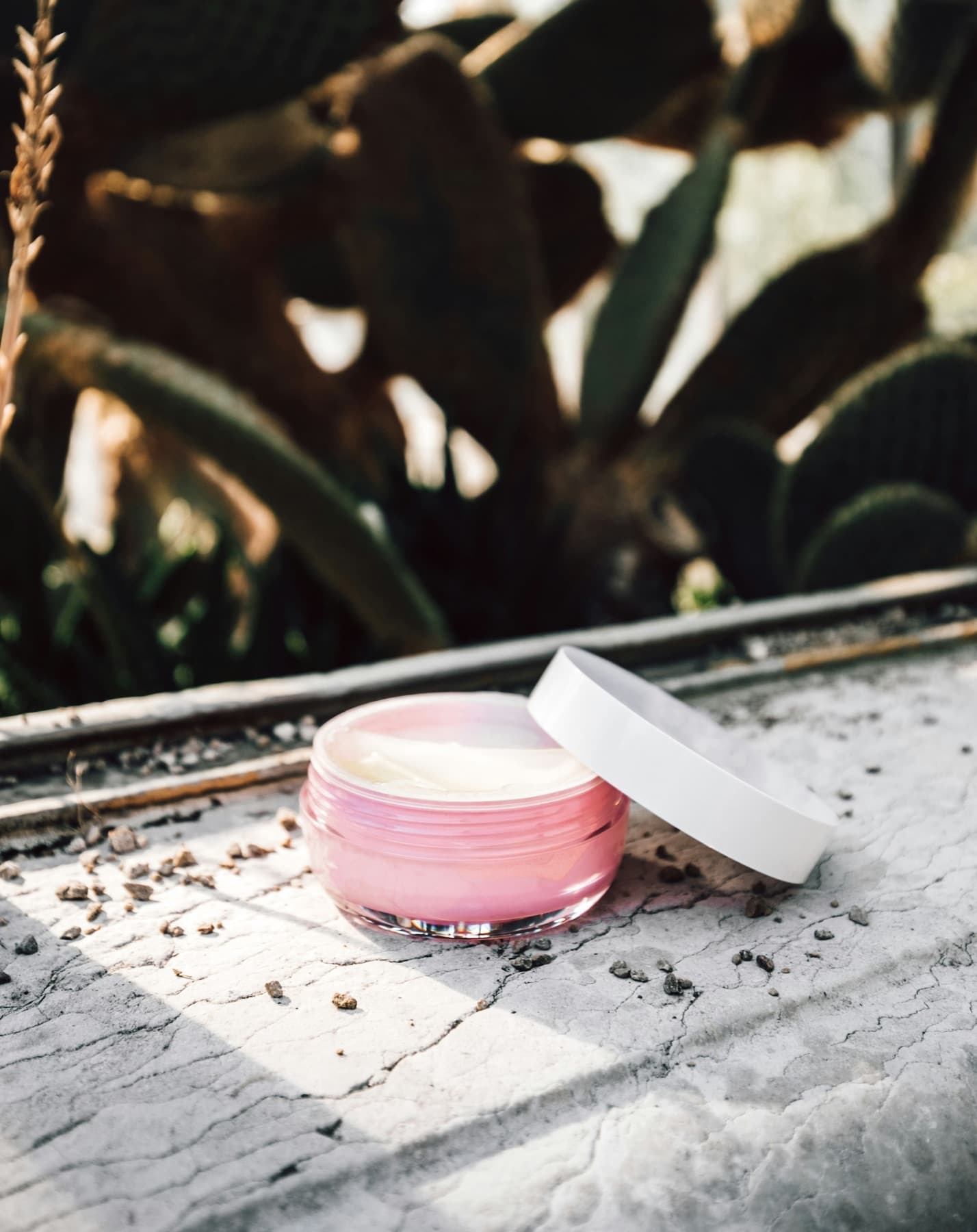 Unlabelled pink glass jar of face cream on a sunlit pale stone ledge