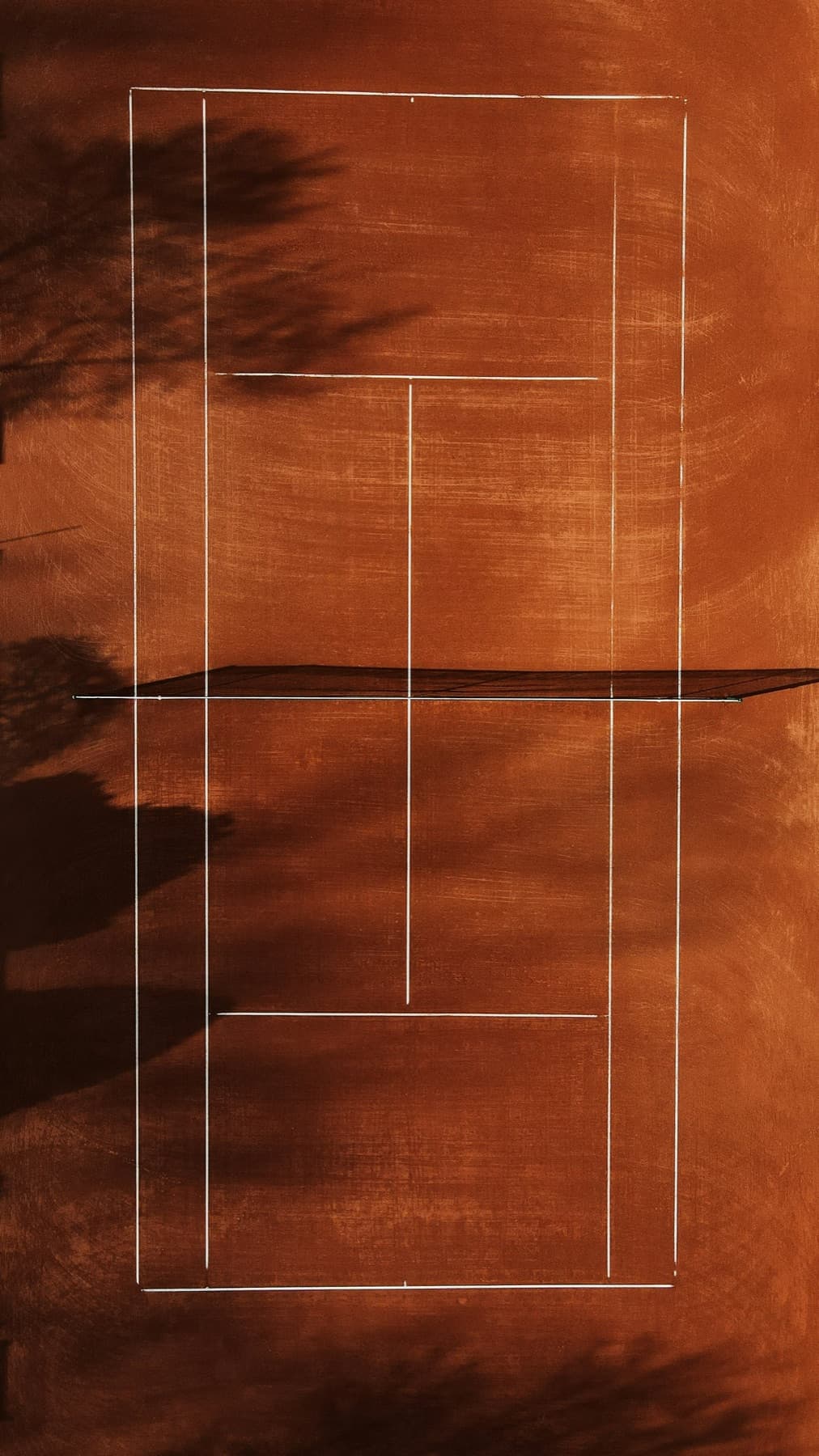 Aerial view of an empty red clay tennis court in Stuttgart with long tree shadows