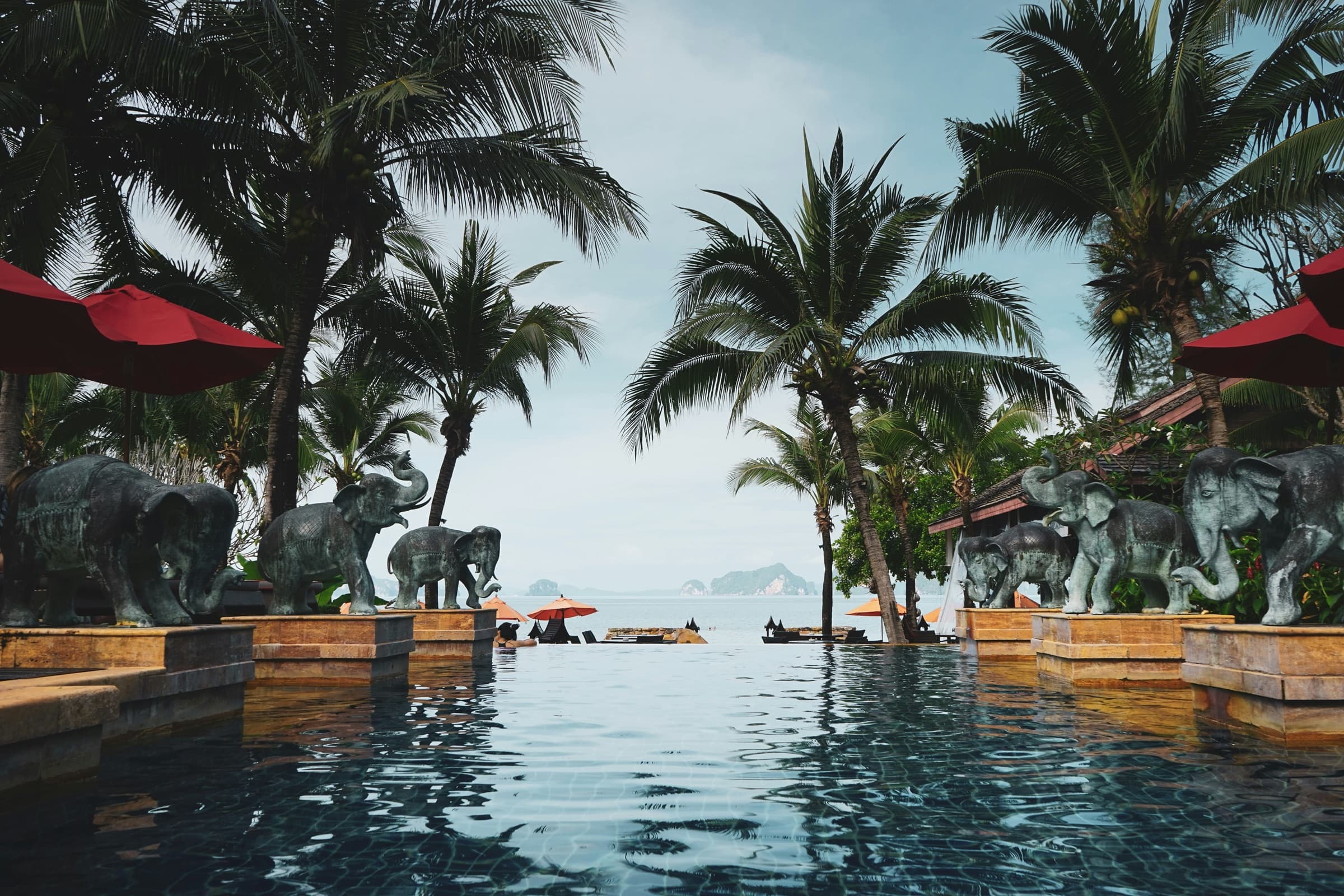 Stone elephant statues lining a palm-fringed resort infinity pool in Krabi, Thailand, looking out to limestone islands in the Andaman Sea