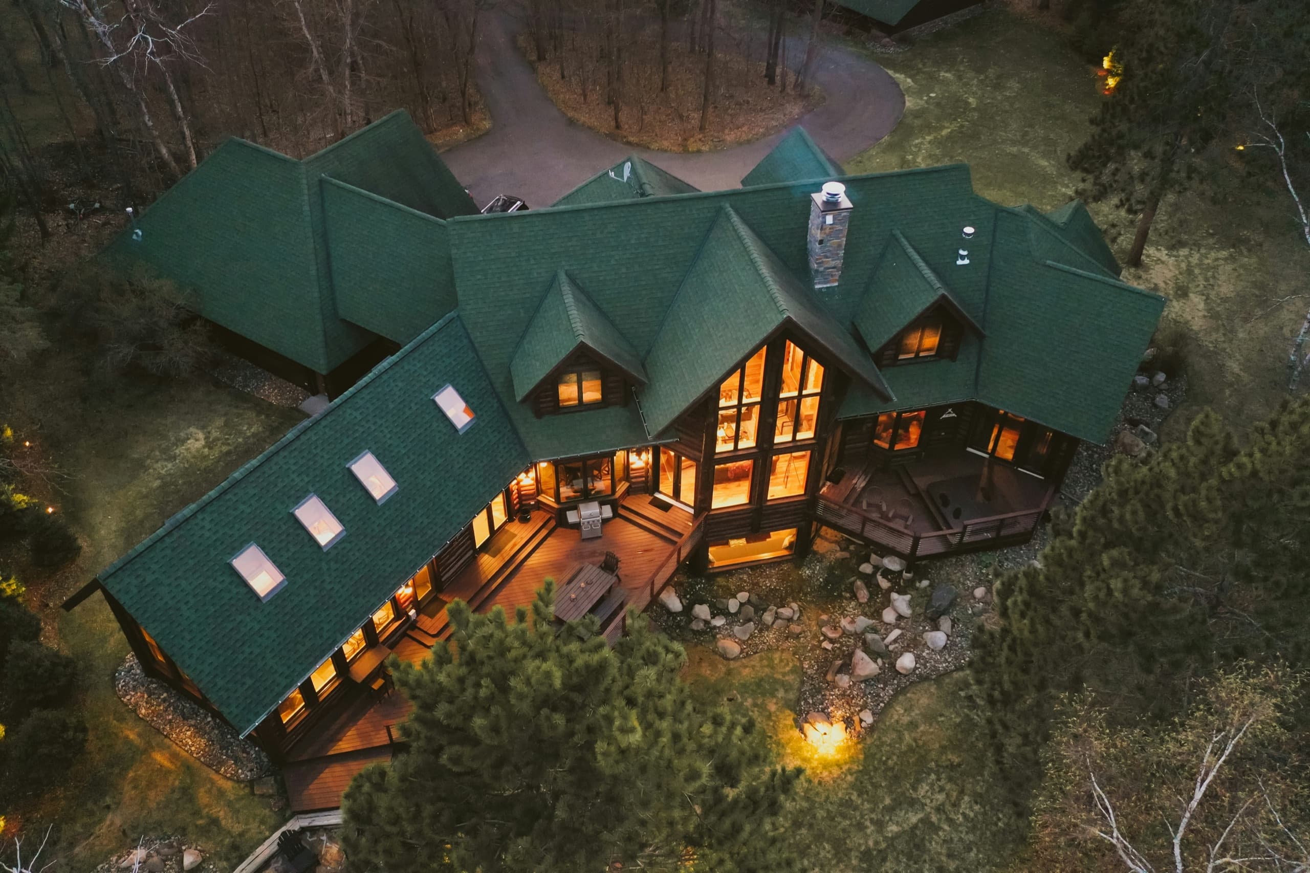 Aerial dusk view of a large lakeside vacation home rental glowing among the trees