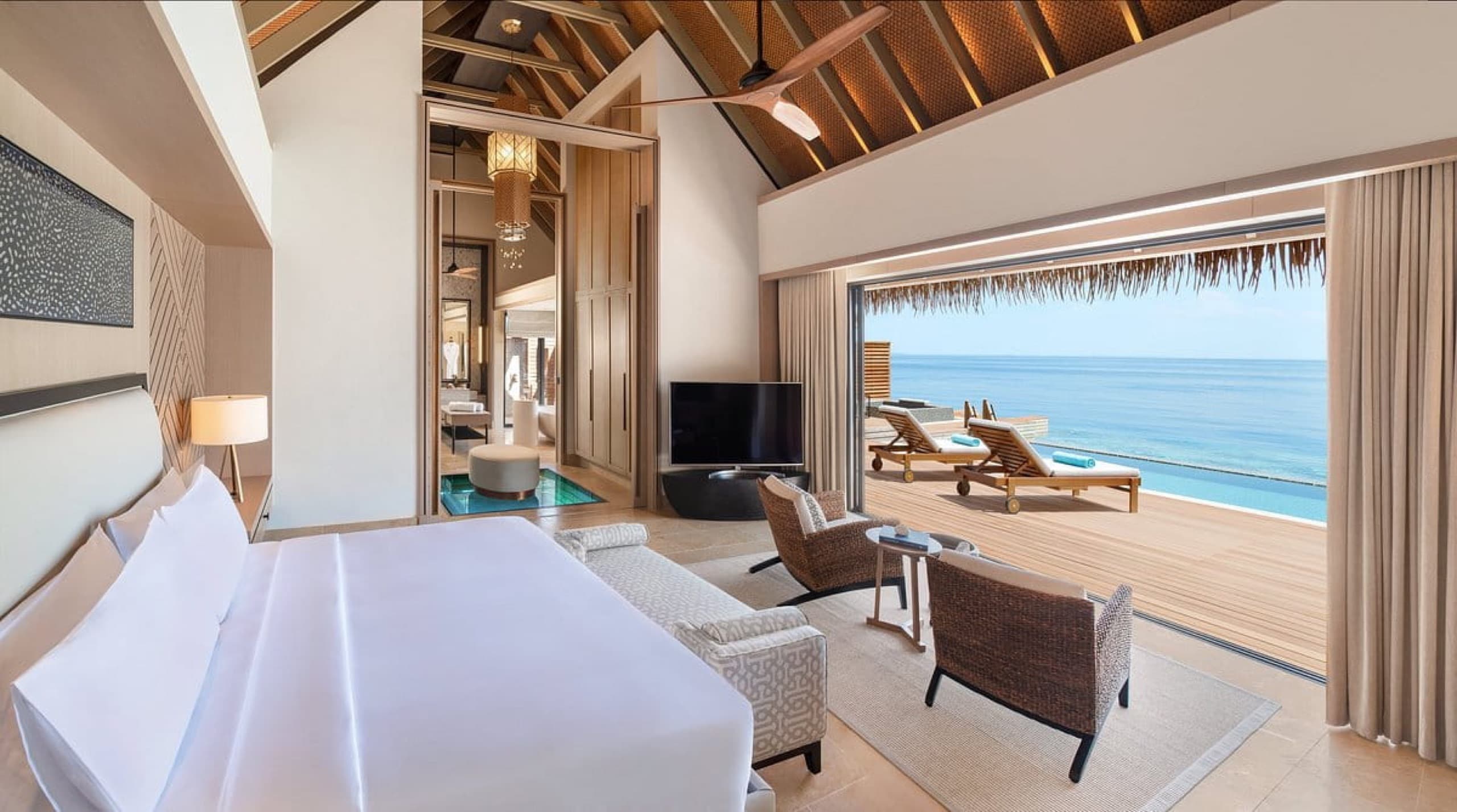 Overwater villa bedroom opening onto a private sun deck and the ocean at Waldorf Astoria Maldives Ithaafushi