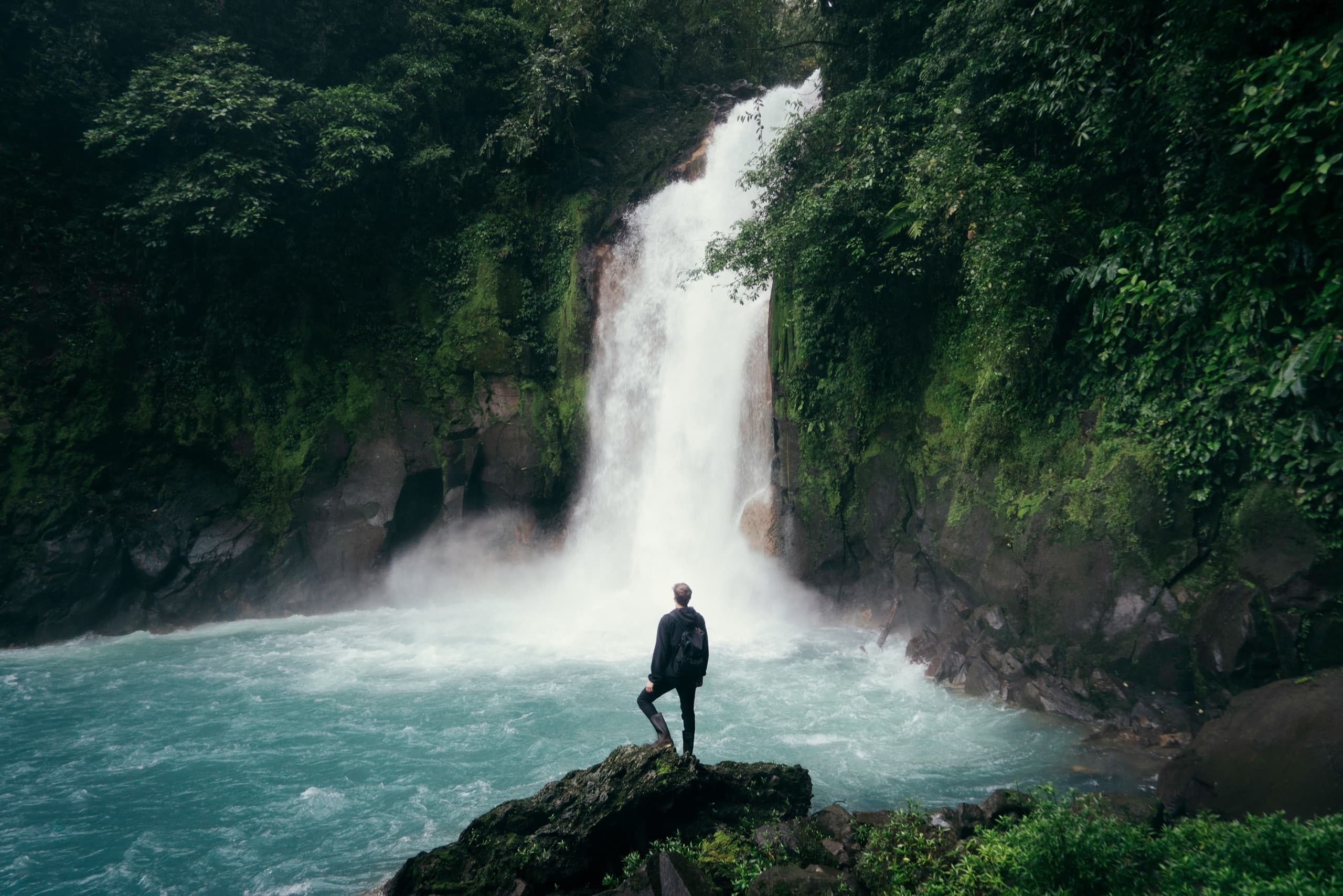Traveler standing before a rainforest waterfall on a guided worldwide tour